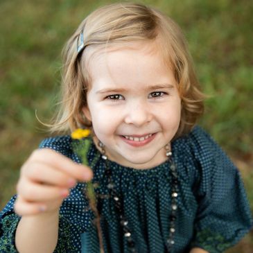Smiling little girl holding a yellow flower.