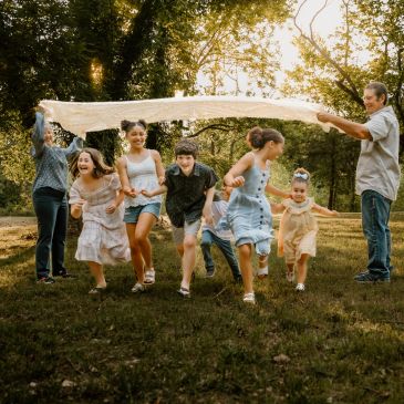 Children running under a cloth held by adults outdoors.