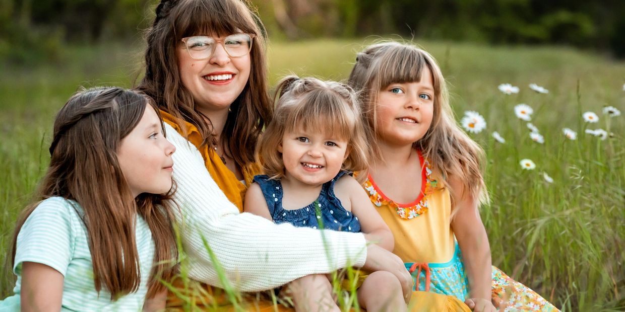 Smiling woman with three happy children in a grassy field.