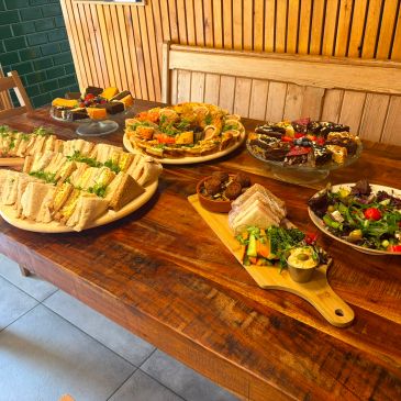 A wooden table set with various sandwiches, salads, and desserts in a cozy dining area.