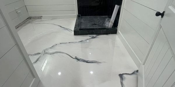 Modern bathroom with glossy marble-like epoxy floor and black tiled shower.