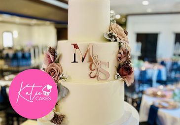 Elegant three-tier wedding cake with floral decorations and initials.
