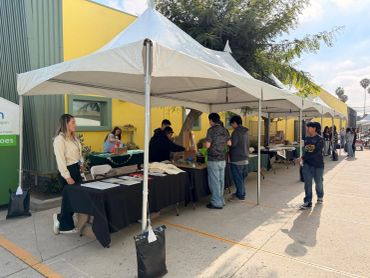 People browsing booths at an outdoor market under white tents.