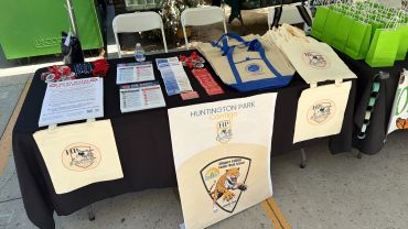 A Huntington Park community event table with informational materials and tote bags.