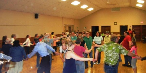 People holding hands and dancing in a large indoor hall.