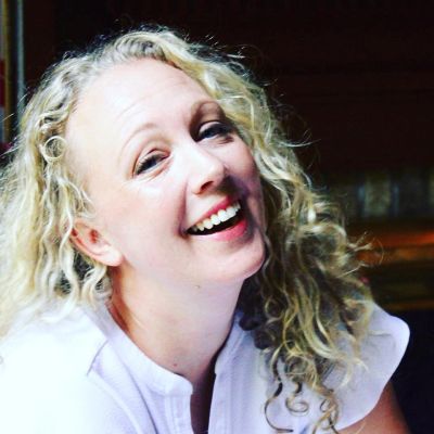 A cheerful woman with curly blonde hair smiling warmly.