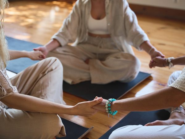 Three people sitting cross-legged holding hands in a circle during a mindfulness session.