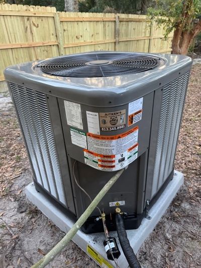Outdoor HVAC unit installed on a concrete pad beside a wooden fence.