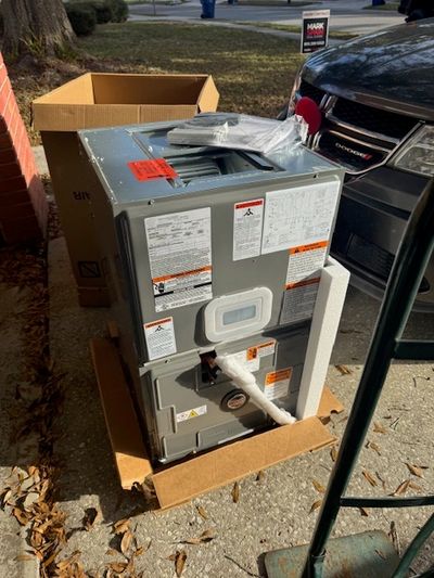New HVAC unit sitting outside in a cardboard box on a driveway.