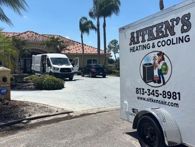 Aitken's Heating &amp; Cooling trailer parked near a residential driveway with palm trees.