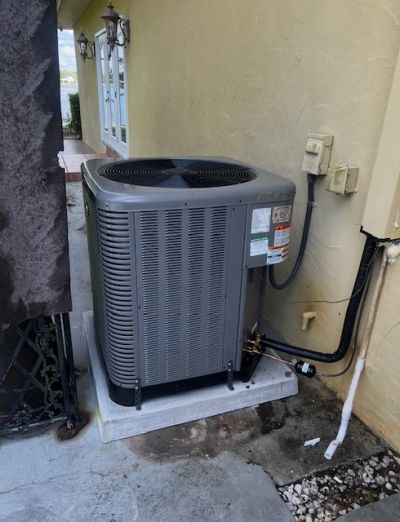 Outdoor air conditioning unit installed on a concrete slab beside a house.