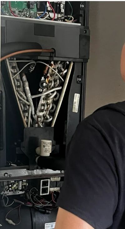 Technician repairing an open HVAC unit with exposed wiring and components.