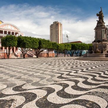 A plaza with black and white wavy patterned pavement, trees, and classical buildings.