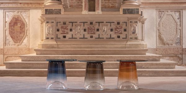 Modern glass table with three colored bases in a classical stone hall.