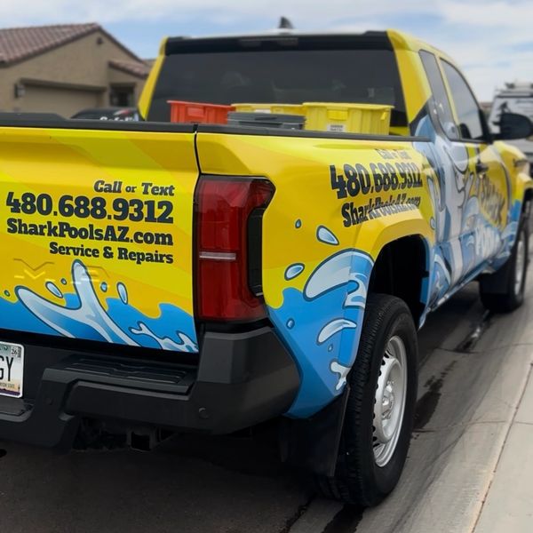 Bright yellow Shark Pools service truck with contact info and water splash graphics.