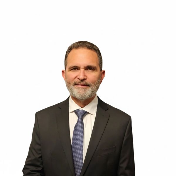 Professional man in a dark suit and tie against a white background.