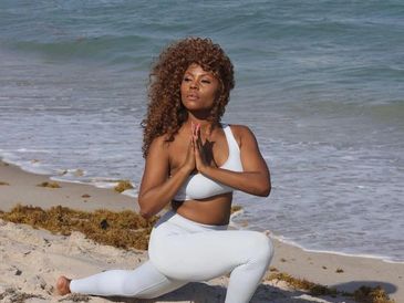 Woman practicing yoga on the beach in white workout attire.