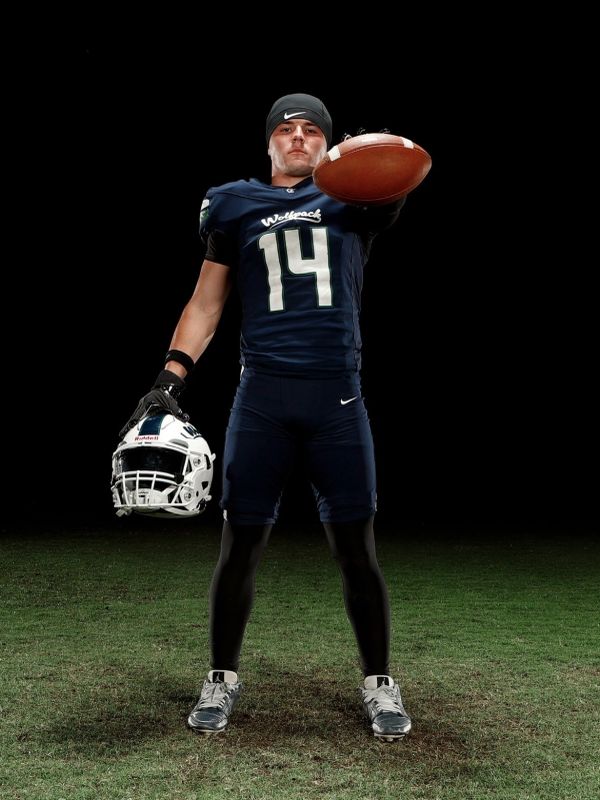 Football player holding helmet and football, looking determined.