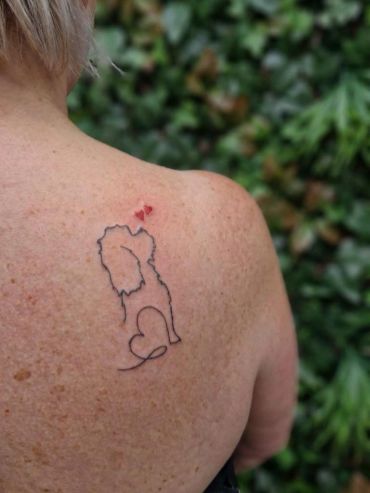 Minimalist lion outline tattoo on shoulder with a small red heart.