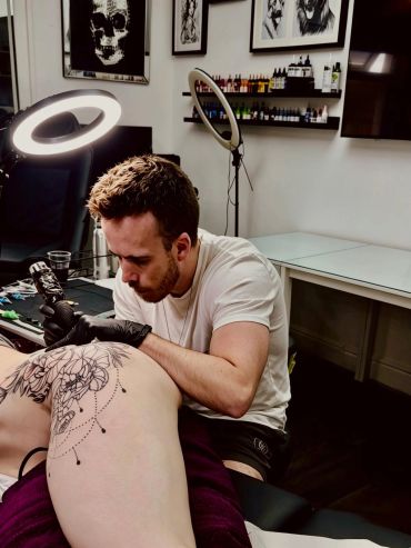 Tattoo artist working on a detailed leg tattoo.