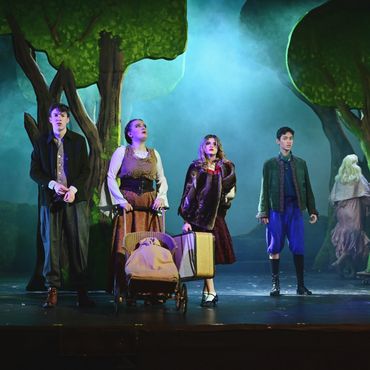 Actors in vintage costumes perform on a forest-themed stage with dramatic lighting.