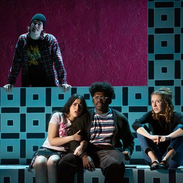Four young people sitting on geometric patterned steps with varied expressions.