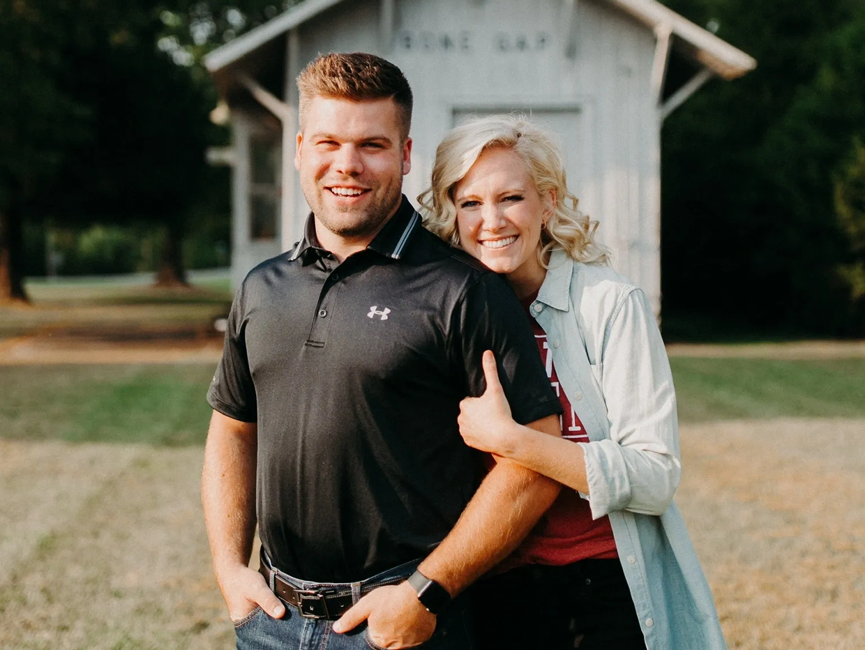 Smiling couple outdoors with woman hugging man from behind.