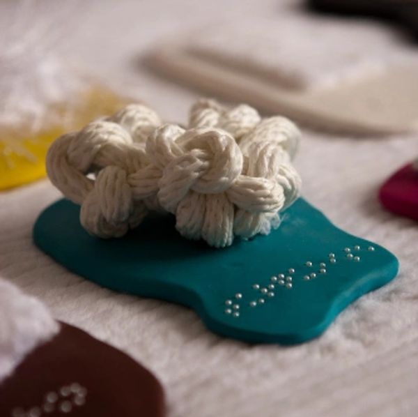 Closeup of a sculpture by Elizabeth. Rope with the word "turquoise" in braille written in pearls. 