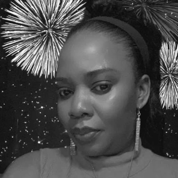 Woman posing with fireworks in the background, wearing earrings and a headband.