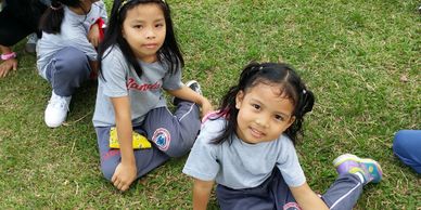 Two young girls sitting on grass, smiling and looking at the camera.