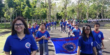 Group of students and a teacher in blue shirts marching with a banner outdoors.