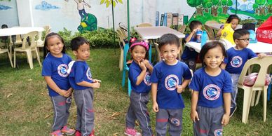 Happy children in matching blue shirts pose outdoors at a school event.