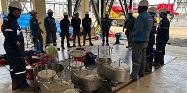 Workers in helmets gathered around industrial equipment indoors.