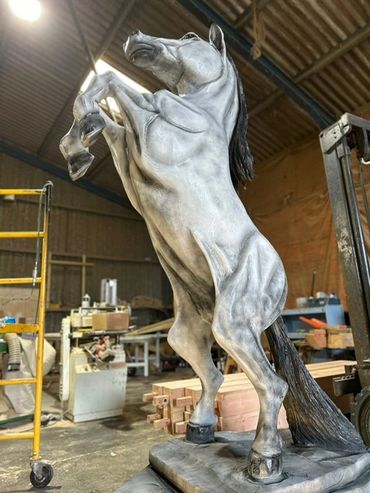 A detailed rearing horse sculpture in an industrial workshop.