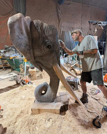 Artist carving a detailed elephant head from wood.