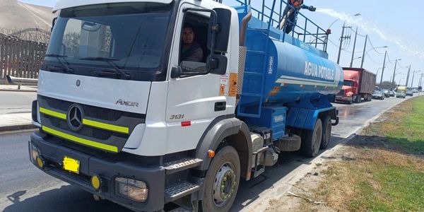 Water tanker truck spraying water on a road with a worker in safety gear.