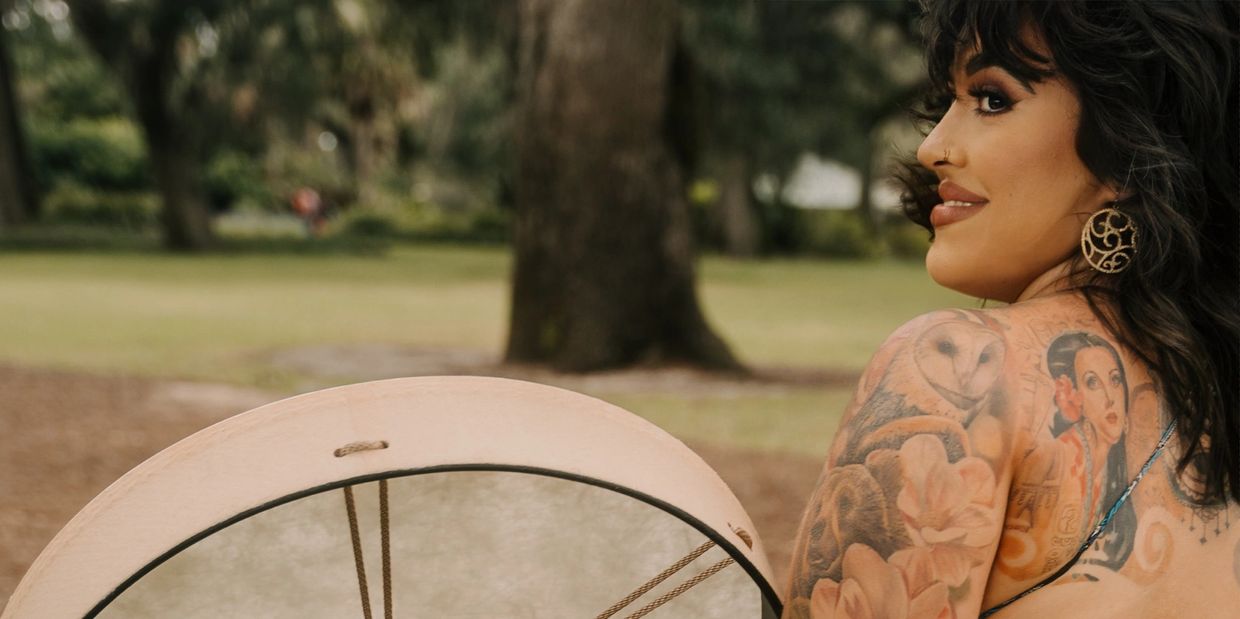 Woman with tattooed back holding a drum outdoors.
