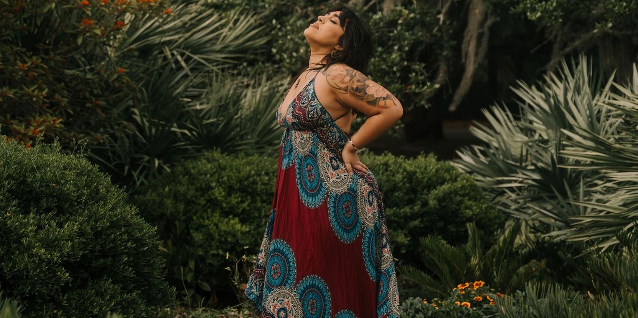 Woman in colorful dress enjoying nature with eyes closed and arms on back.