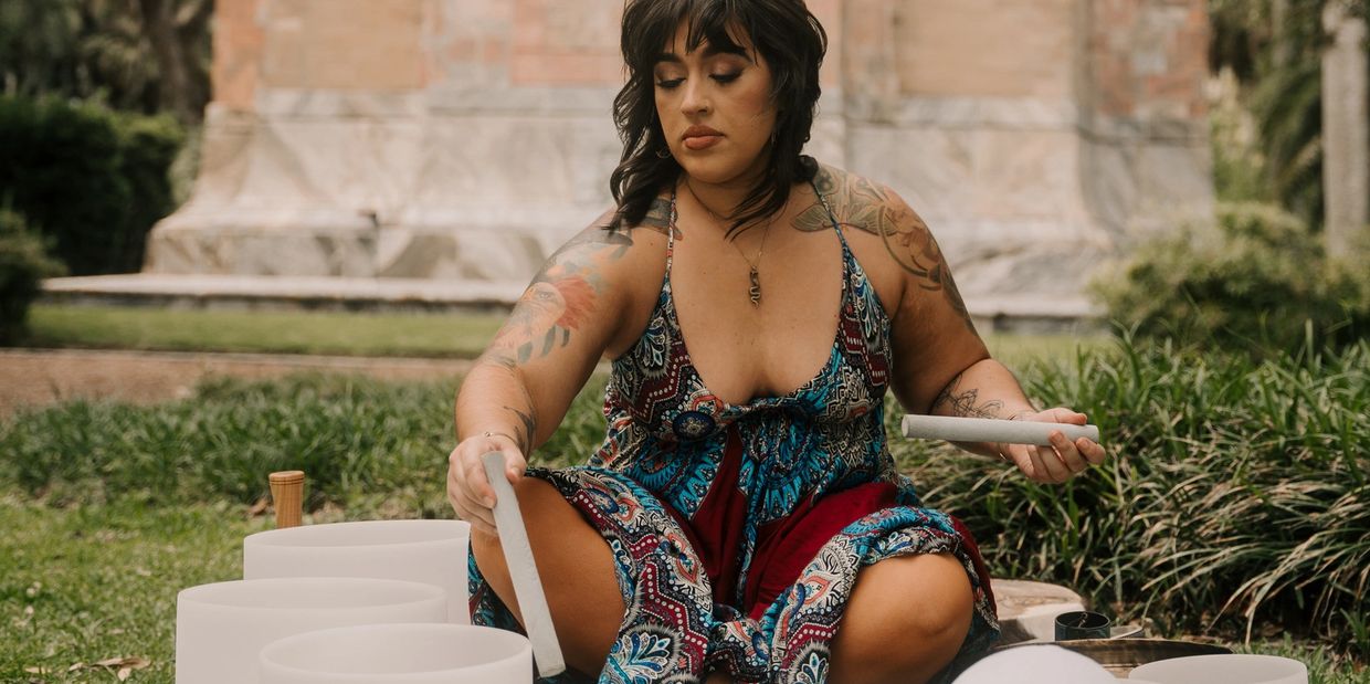Woman in colorful dress playing crystal singing bowls outdoors.