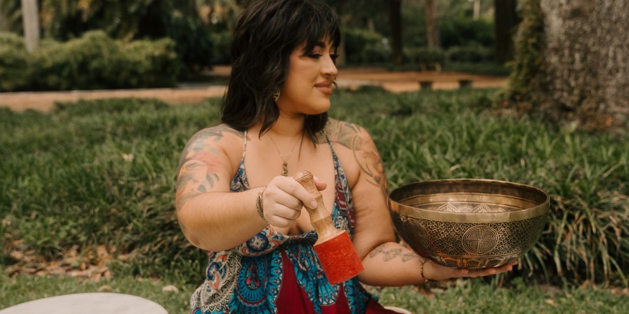 Woman holding a Tibetan singing bowl and mallet outdoors.