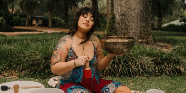 Woman playing a singing bowl outdoors in a peaceful setting.