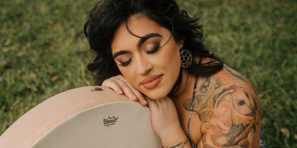Woman with a tattoo resting her head on a drum outdoors.