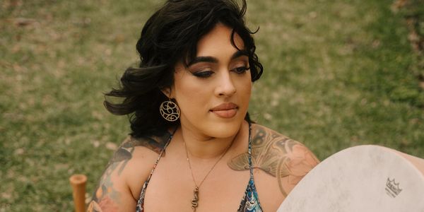 Woman with tattoos and earrings holding a drum outdoors.