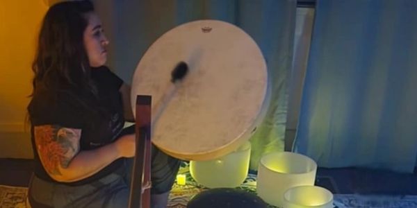 Woman playing a large drum in a dimly lit room with glowing bowls.