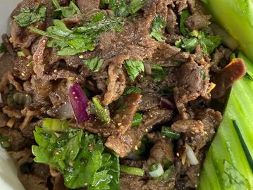 Bowl of seasoned beef with herbs, onions, and cucumber slices on rice.
