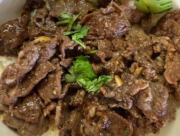 Bowl of savory grilled beef over white rice garnished with cucumber and cilantro.