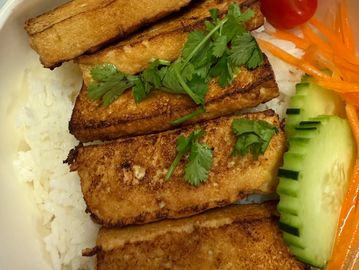 Grilled tofu on white rice with fresh vegetables and herbs.