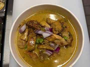 Bowl of creamy chicken curry garnished with chopped onions and green herbs.