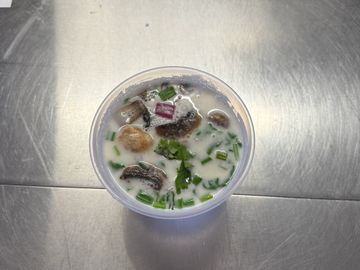 Creamy soup with mushrooms and herbs in a plastic container.