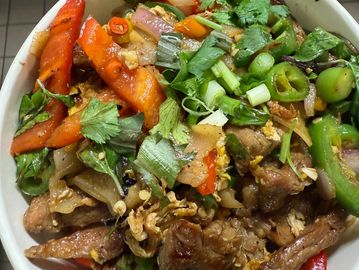 A colorful bowl of stir-fried beef with vegetables and fresh herbs.